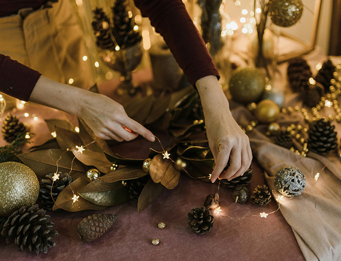 Hands arranging holiday decor with pine cones and lights on a festive table, creating a warm Christmas atmosphere. Hands arranging holiday decor with pine cones and lights on a festive table, creating a warm Christmas atmosphere.