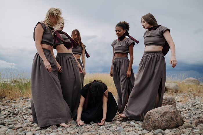 A group of women on a rocky beach, wearing matching gray outfits, with one kneeling on the ground.