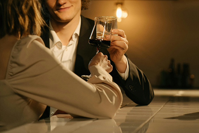 Couple toasting with wine, capturing a moment related to the dating trend "Throning" at a dimly lit bar.