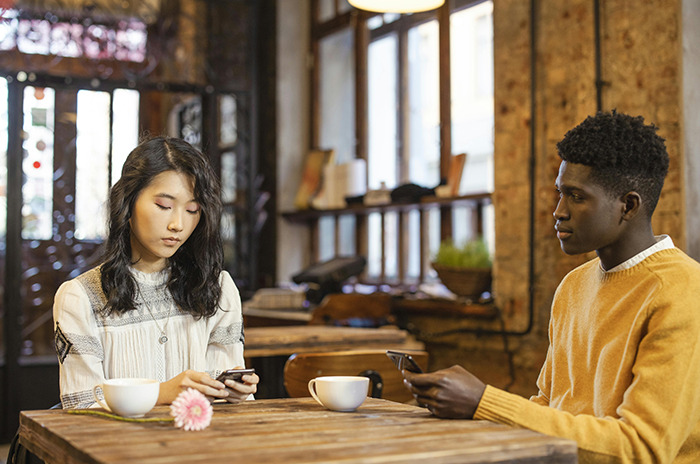 Two people using phones at a caf&eacute; table with coffee cups.
