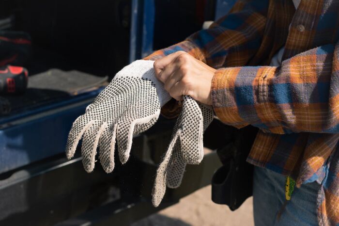 Person in a plaid shirt puts on safety gloves, standing near a vehicle, focused on a task requiring precaution.