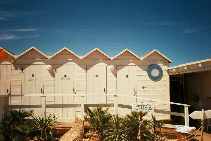 Beach huts under clear blue sky, representing a nudist lifestyle setting.