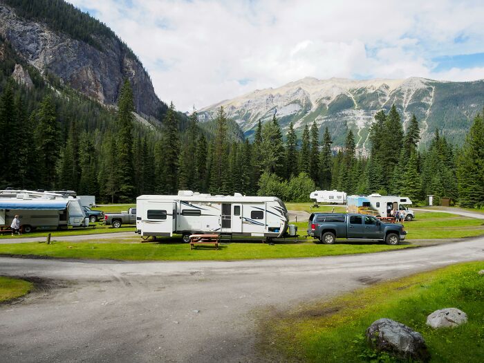RVs parked in a lush campsite surrounded by mountains, with people embracing a nudist lifestyle.