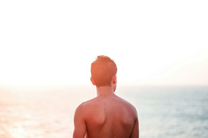 Man enjoying the nudist lifestyle, gazing at the ocean during sunset.