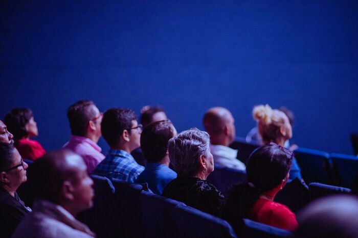 Audience seated in a theater, listening attentively, representing unexpected escalations from a "You Up?" text.