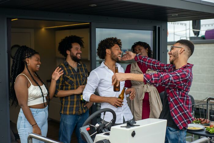 Friends laughing and holding drinks, embodying moments of lighthearted cringe at a rooftop gathering.