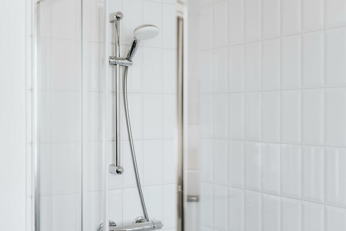 Showerhead with white tiles exemplifies frugal home hacks, offering luxury without high costs.