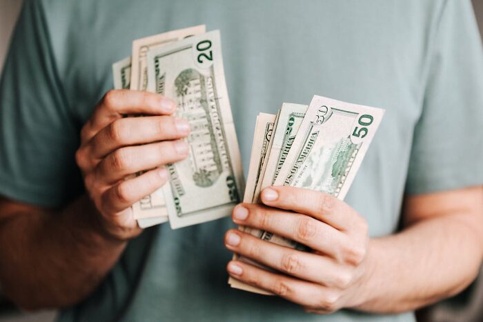Person counting dollar bills in hands, wearing a green shirt, related to spending decisions.