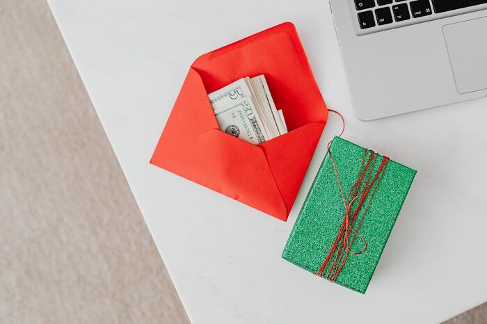 Red envelope with cash and a green gift box on a white table near a laptop, representing signs of a good person.