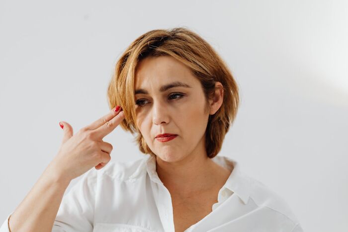 Woman in a white shirt making a gesture with her fingers, expressing frustration related to cringy nice guy stories.