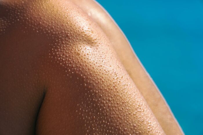 Close-up of tanned skin with water droplets, representing a nudist lifestyle by the pool.