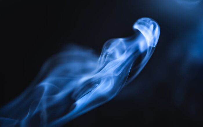 Blue smoke swirling against a dark background, illustrating abstract forms.