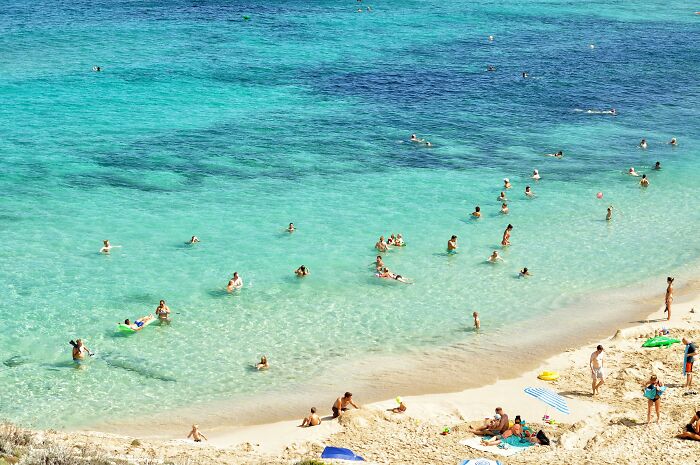 People enjoying a nudist lifestyle on a sunny beach, swimming and relaxing by the clear blue water.
