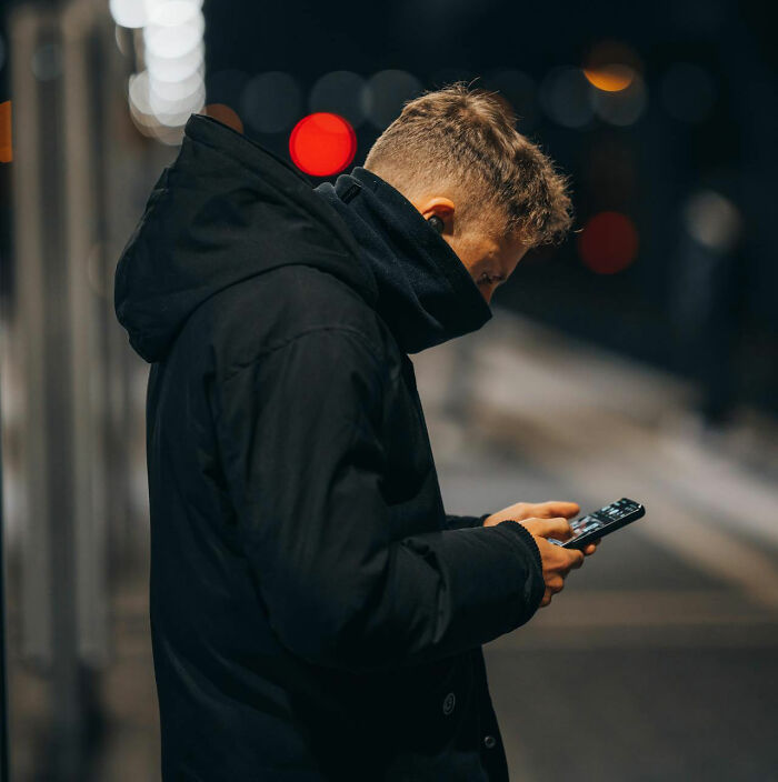 Man in dark coat using phone at night, illustrating tense moments.