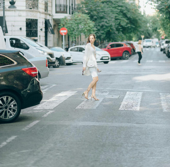 Woman in white dress crossing the street, looking back, symbolizing a moment realized dating an idiot.