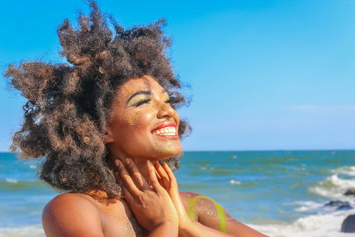 A smiling person enjoys the beach, embodying the nudist lifestyle under a bright blue sky.