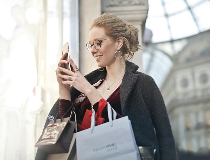 Woman smiling at phone while shopping, capturing the essence of throning in a casual urban setting.