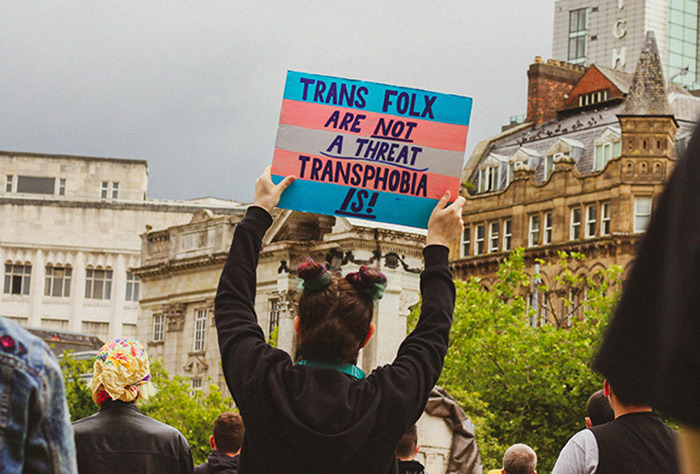 Protester holding a sign about trans rights amidst city buildings, reacting to JK Rowling's comments.