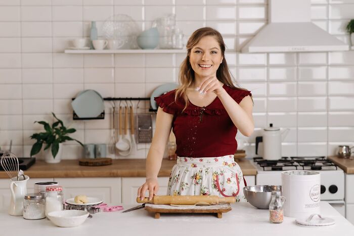 Person baking in a kitchen, smiling while rolling dough, illustrating people list trends for 2024.