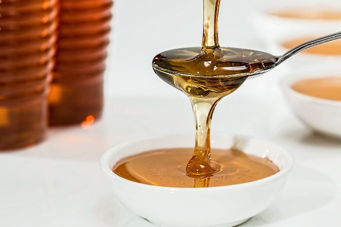 Honey being poured from a spoon into a small white dish, showcasing its golden color and smooth texture.