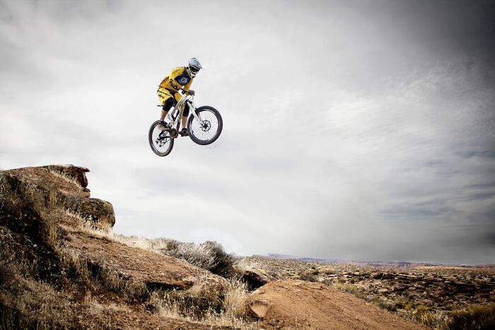 A person on a mountain bike jumps over a rocky terrain under a cloudy sky.
