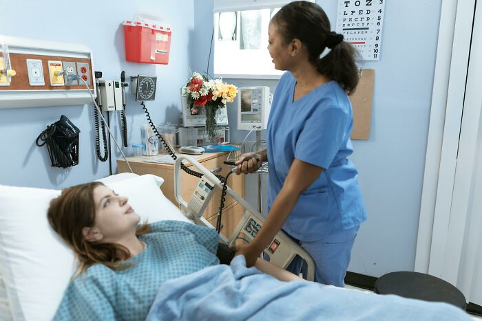 Nurse in blue scrubs assists a patient in a hospital room, highlighting changes in occupations over the years.