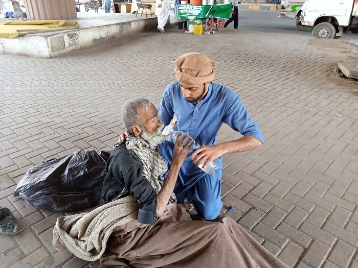 A compassionate person helping an older man by giving him water, demonstrating a small act of kindness.