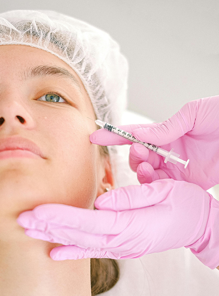 Person receiving Botox injection, healthcare professional wearing pink gloves and a hair cap.