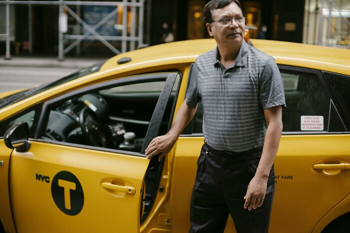 Man standing beside a yellow NYC taxi, illustrating changing occupations.