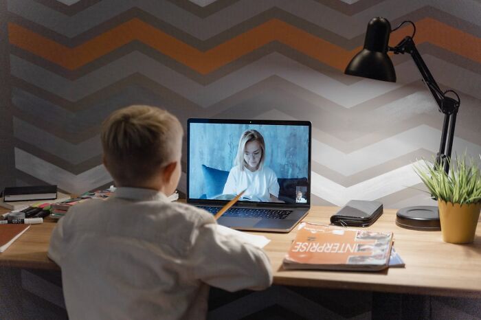 Child in virtual class, learning secrets about jobs, at a wooden desk with a lamp and magazines.