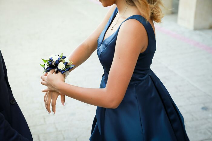 Person in a blue dress adjusting a floral corsage on their wrist, symbolizing a lost friendship moment.