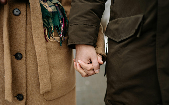 Two people holding hands in winter coats, illustrating the dating trend "throning.