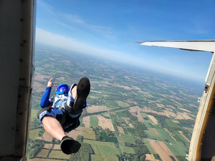 Skydiver in blue gear freefalling from plane against a scenic landscape backdrop.