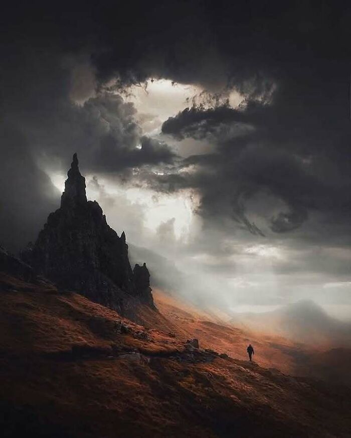 Dramatic Scottish landscape with dark clouds and a lone traveler on a rugged path near towering rock formations.