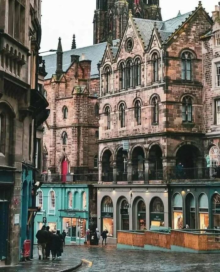 Historic stone buildings in Edinburgh, Scotland, with a cobblestone street and colorful shops below.