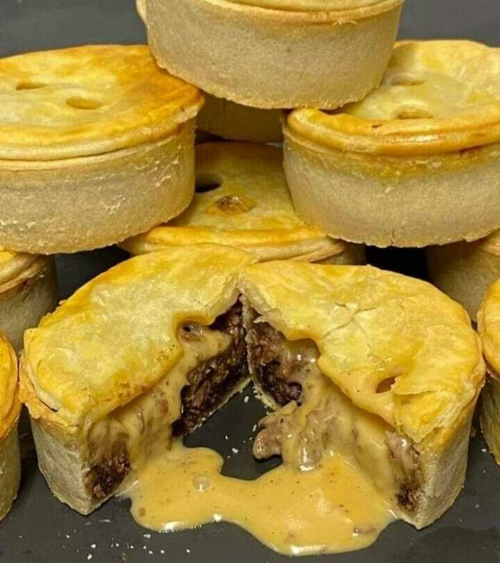 A stack of Scottish meat pies with one cut open, revealing a savory filling, illustrating traditional Scottish cuisine.