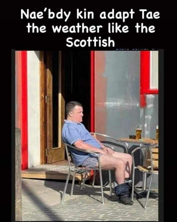 Man enjoying Scottish weather humorously in a T-shirt and shorts, beer on table, embodying Scottish adaptability.