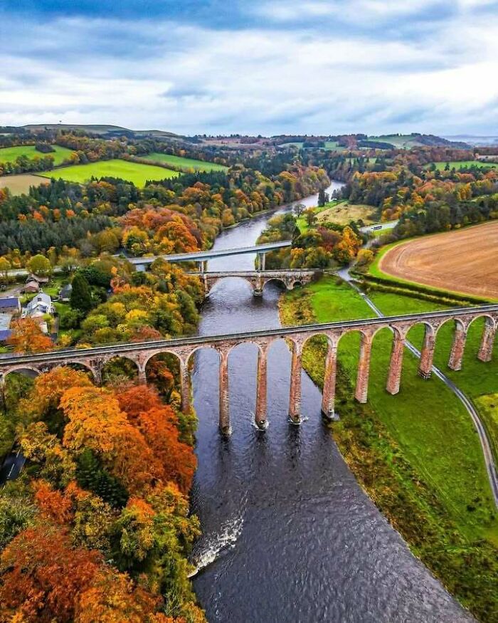 Aerial view of picturesque viaducts over a river surrounded by autumn foliage in Scotland.