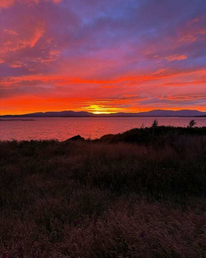 Vibrant Scottish sunset over a tranquil loch with silhouetted hills and colorful sky.