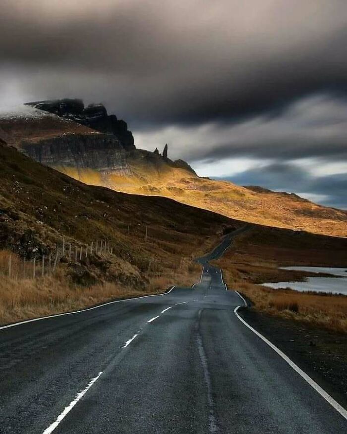 Scenic winding road through rugged Scottish landscape under dramatic skies.