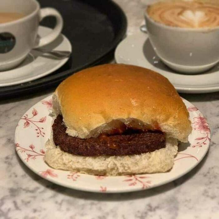 Scottish humor showcased in haggis burger on floral plate with coffee cups, capturing Scotland's quirky essence.