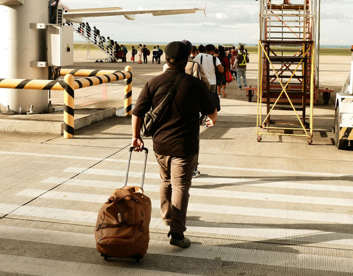Man with suitcase walking on airport tarmac, boarding a plane, ignoring the child&rsquo;s tantrum situation on flight.