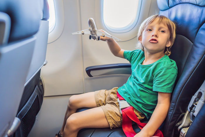 Child with toy plane in airplane seat, green shirt, looking out window.