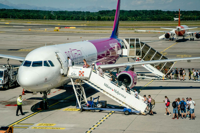 Passenger boarding a purple and white airplane at the airport, showing travel preparation and operational activities.
