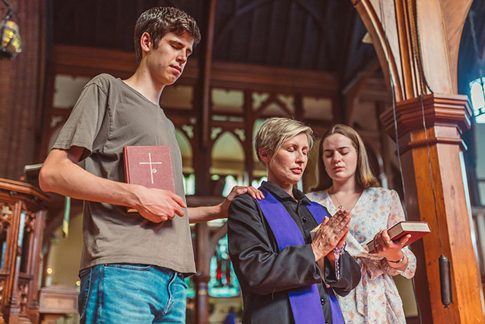 A woman in church with two others, holding a Bible and rosary, symbolizing Christian faith and devotion.