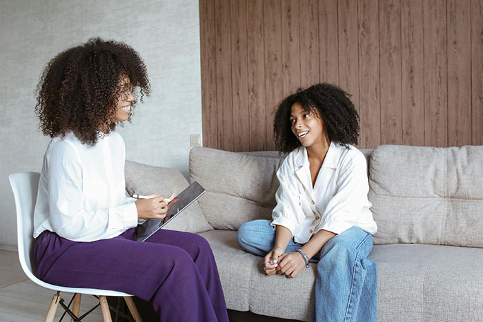 Two women having a discussion on a sofa, one writing notes.