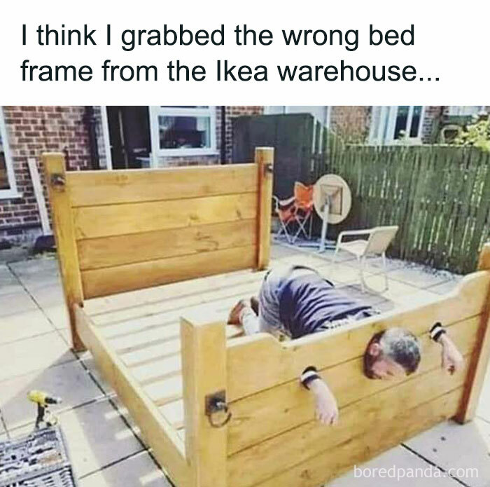 Man humorously trapped in a giant wooden bed frame outdoors.