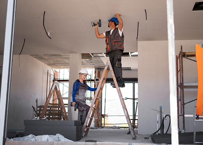 Construction workers on ladders fixing a ceiling, showcasing reality TV shows behind-the-scenes dynamics.