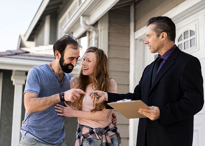 Couple receiving keys from realtor, smiling and standing outside their new home, reality TV decision moment.
