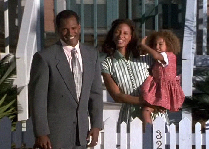 A smiling family stands behind a white picket fence, capturing a moment reminiscent of reality TV shows.